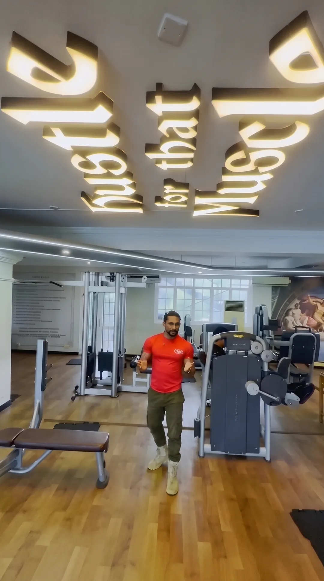 The main training floor, a trainer, and a lit sign reading hustle for that muscle